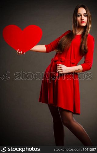 Valentines Day. Woman in red dress holding heart sign love symbol on grey background in studio.