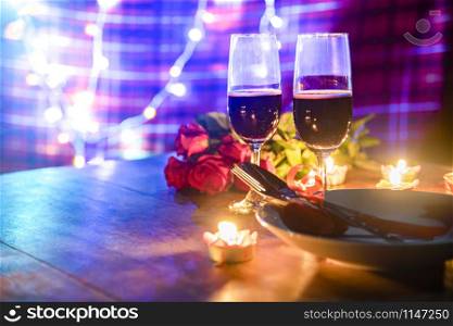 Valentines dinner romantic love concept / Romantic table setting decorated with fork spoon on plate and couple champagne glass roses with candlelight on wooden table dinner night light background