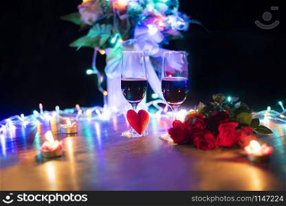 Valentines dinner romantic love concept / Romantic table setting decorated with red heart and couple champagne glass roses with candlelight on wooden table dinner night light background