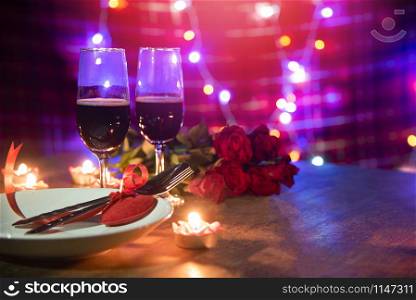 Valentines dinner romantic love concept / Romantic table setting decorated with Red heart fork spoon on plate and couple champagne glass wine roses with candlelight on wooden table dinner at night
