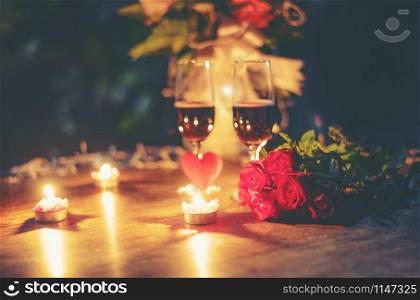 Valentines dinner romantic love concept / Romantic table setting decorated with Red heart and couple champagne glass roses flower with candlelight on wooden table dinner at night outdoors tone vintage