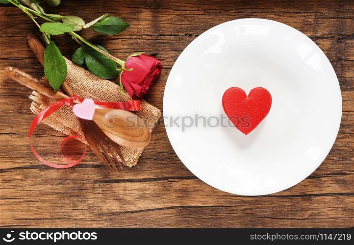 Valentines dinner romantic love food and love cooking concept / Red heart on white plate romantic table setting decorated with wooden spoon fork and rose on rustic background