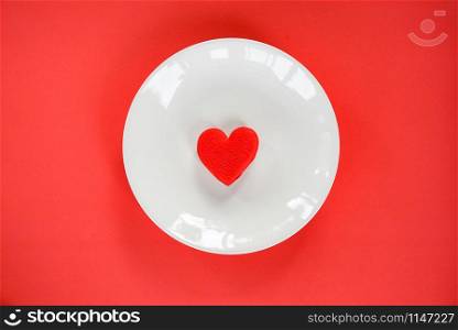Valentines dinner romantic love food and love cooking concept / Red heart on white plate romantic table setting decorated on red texture background top view