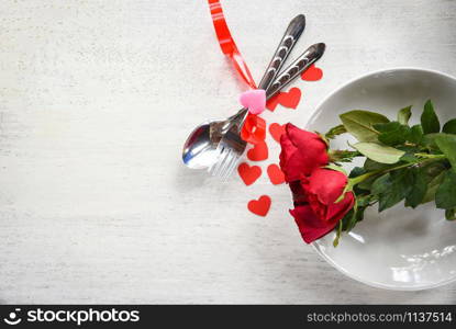 Valentines dinner romantic love food and love cooking concept - Romantic table setting decorated with fork spoon red heart and roses on plate with white wooden texture background top view copy space