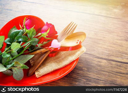 Valentines dinner romantic love food and love cooking concept - Romantic table setting decorated with wooden fork spoon roses in red heart plate on rustic background