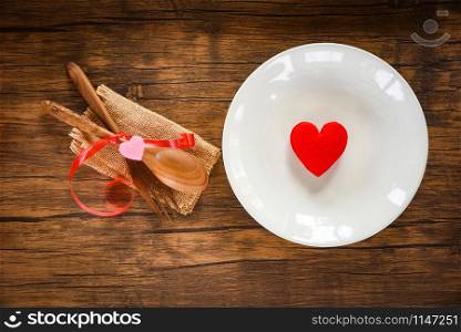 Valentines dinner romantic love food and love cooking concept - Romantic table setting decorated with wooden fork spoon and red heart on plate on dining table background