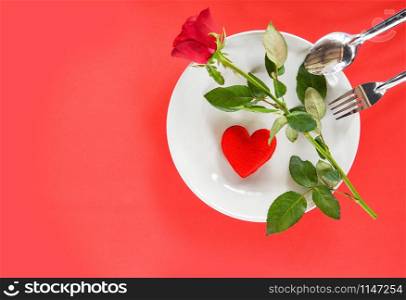 Valentines dinner romantic love food and love cooking concept - Romantic table setting decorated with fork spoon red heart and roses on plate on red background top view copy space
