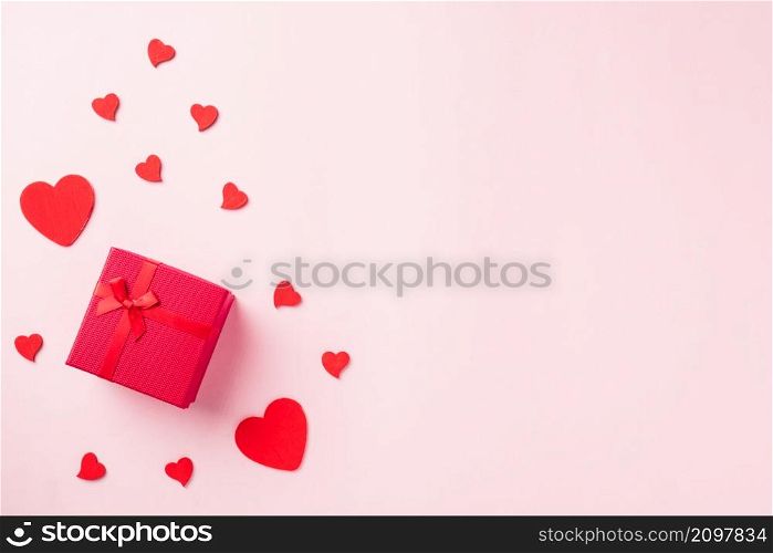Valentines&rsquo; day background. Red gift box with ribbon bow and wood red hearts shaped composition greeting card for love isolated on pink background with copy space. Top View from above