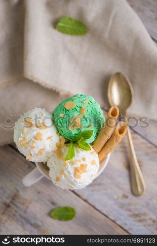 Vanilla and mint ice cream in cup on wooden vintage style background.