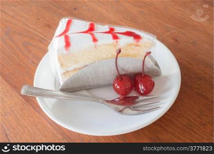 Vanilla cake with cherry on wood background