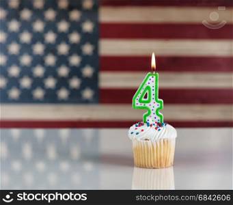Vanilla cupcake and number four candle with rustic wooden United States Flag in background. July 4th holiday concept