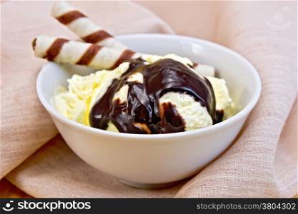 Vanilla ice cream in a bowl with wafer rolls and chocolate syrup on a napkin on the background of wooden boards