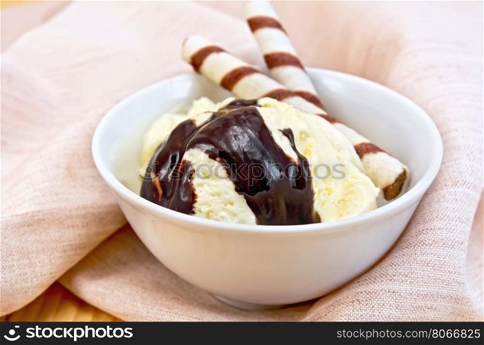 Vanilla ice cream in a white bowl with wafer rolls and chocolate syrup on a napkin against the background of wooden boards