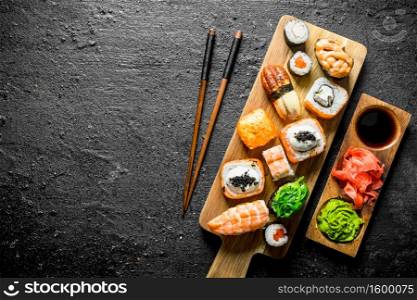 Variants of types of sushi, rolls and maki on a cutting Board with sticks. On black rustic background. Variants of types of sushi, rolls and maki on a cutting Board with sticks.