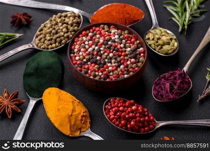 Variation of spices in metal spoons paprika, turmeric, cardamom, a mixture of allspice, thyme, rosemary and salt on a dark concrete background