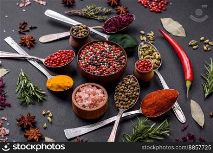 Variation of spices in metal spoons paprika, turmeric, cardamom, a mixture of allspice, thyme, rosemary and salt on a dark concrete background