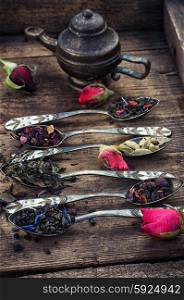 Varieties of dry tea. Dried tea leaves in spoons on stylish background of the teapot.