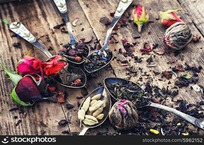 Varieties of dry tea. Varieties of tea brewed in an iron spoon on wooden background with buds of tea roses