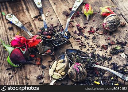 Varieties of dry tea. Varieties of tea brewed in an iron spoon on wooden background with buds of tea roses