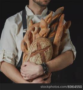 Variety of bread in hands of baker. Baker keeps a variety of bread