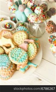Variety of colorful cake pops and cookies on white wooden desk