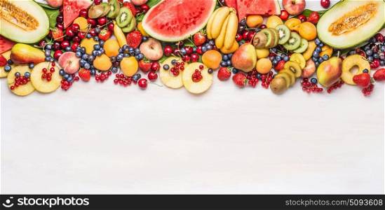 Variety of colorful organic fruits and berries on white table background, top view, border. Healthy food and vegetarian eating concept