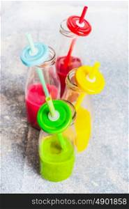 Variety of colorful smoothies in bottles with drinking Straws: green,yellow,red.