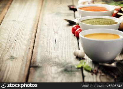 Variety of cream soups - tomato, broccoli and pumpkin soups over wood background. Copy space