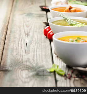 Variety of cream soups - tomato, broccoli and pumpkin soups over wood background. Copy space