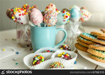 Variety of decorated candies, cake pops and cookies on white wooden desk