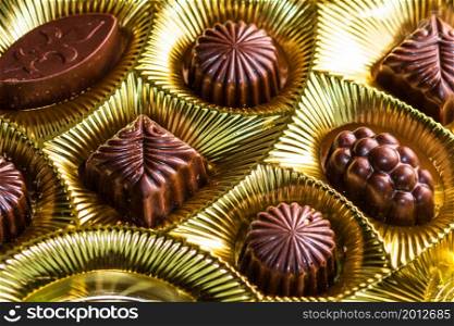 Variety of delicious chocolate pralines in a golden box. Close up of bonbons, selective focus.