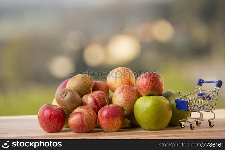 variety of fruits and a shopping cart on a wooden table, outdoor