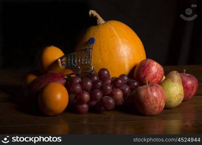 variety of fruits and a small shopping cart on a woden table, studio picture