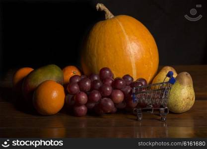 variety of fruits and a small shopping cart on a woden table, studio picture