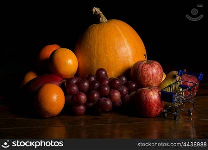 variety of fruits and a small shopping cart on a wooden table, studio picture