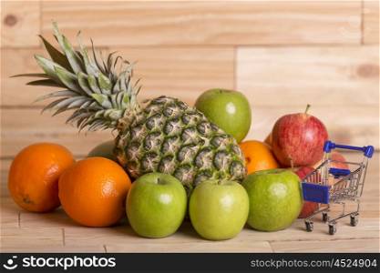 variety of fruits and a small shopping cart on a wooden table, studio picture