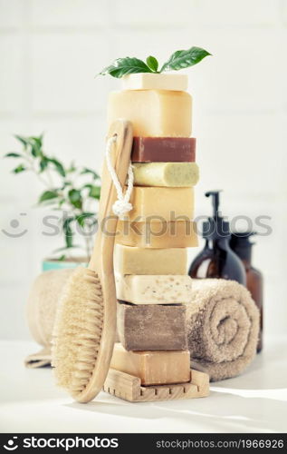 Variety of natural organic handmade soap bars on white bathroom countertop, wooden massage brush, towel and scincare accessories