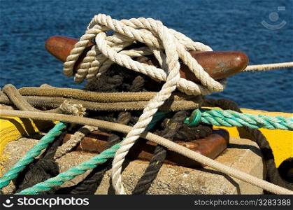 Variety of ropes tied to cleat on fishing pier.