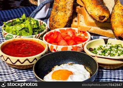 Variety of salad ingredients, tomatoes sauce, tasty fried egg and raw vegetables for healthy breakfast