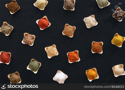 Variety of spices and herbs in bowls, a pattern on a black background. Flat lay of condiments background. Above view with flavors. Cooking frame.