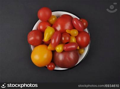Variety of tomato cultivars in enamel bowl on black background