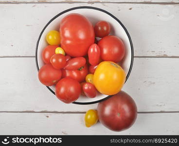 Variety of tomato cultivars in enamel bowl on weathered wood