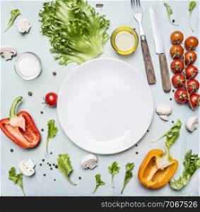 variety of vegetables laid out around a white plate with oilknife and fork on wooden rustic background top view close up