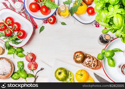 Variety on colorful tomatoes with flavoring and salad ingredients in enamelled bowls for tasty summer cooking on light wooden background, top view, frame