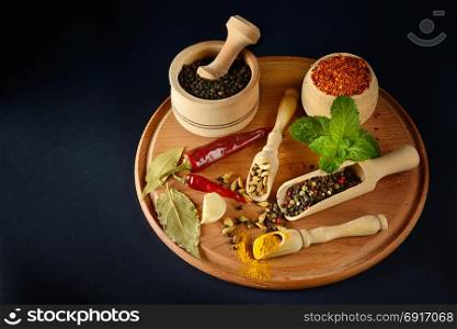 Variety spices and peanuts in wooden spoons and cups on black background. Free space for text. Top view.