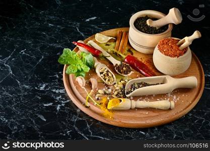 Variety spices in wooden spoons and cups on black background. Free space for text. Top view.