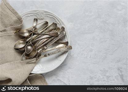 Various antique silverware on ceramic plate on the background of gray concrete surface, with copy-space