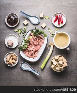 Various asian cooking ingredients in bowls for spicy asian soup with tofu and meat : sliced meat, ginger, chili, diced tofu ,Oyster sauce, garlic and broth, top view, flat lay