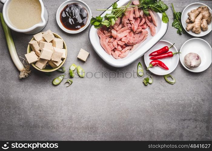 Various asian cuisine ingredients with tofu and meat for tasty cooking on gray stone background, top view, border