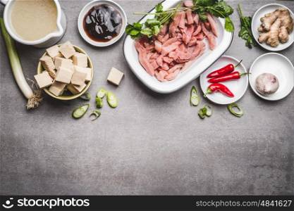 Various asian cuisine ingredients with tofu and meat for tasty cooking on gray stone background, top view, border